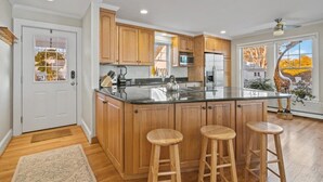 A modern kitchen with wooden cabinets, a large island with stools, a refrigerator, and a microwave. - Charming beach home, complete with pool & cozy guest house! (Clinton)