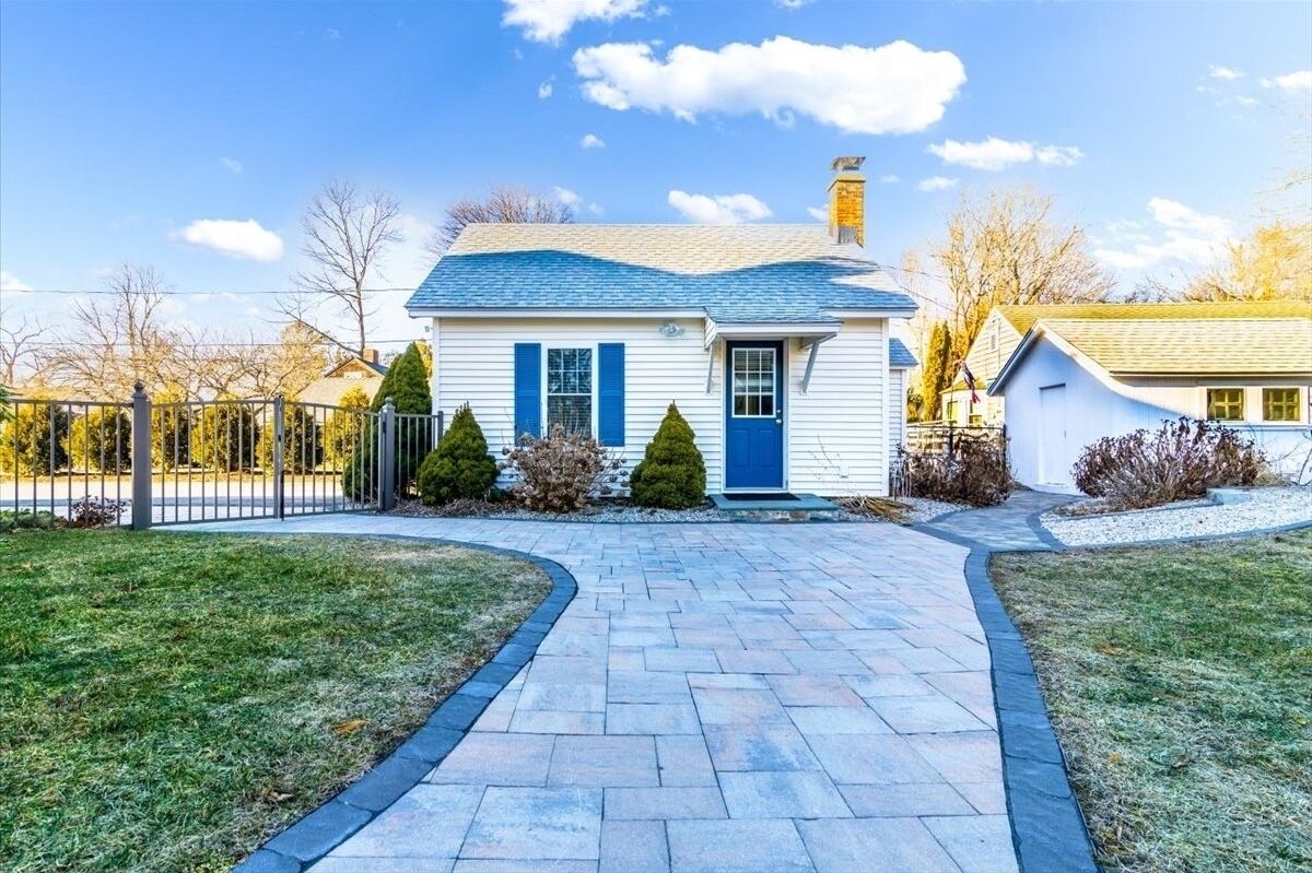 A single-story house with a blue door and shutters, a paved driveway, and a small front yard with trimmed bushes.