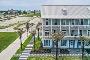 Un immeuble à plusieurs étages, doté d’une façade blanche et de touches de couleur bleue, situé près d’une plage, avec une promenade pavée et des palmiers.