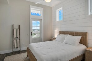 Une chambre avec un grand lit, une échelle en bois, une porte blanche et une fenêtre.