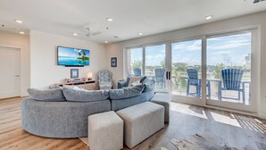 Ein modernes Wohnzimmer mit einem Ecksofa, einem Flachbildfernseher und einer großen Schiebeglastür, die auf einen Balkon mit Sitzgelegenheit führt.