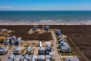 An aerial view of a coastal residential area with houses, a beach, and a road.