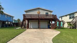 Ein zweistöckiges Haus mit einer überdachten Garage, einer Holzterrasse und einer Treppe, die zum oberen Stockwerk führt.