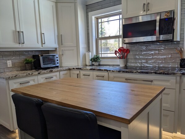A modern kitchen with white cabinets, a wooden island, a built-in microwave, and a window with a view. - Charming Home Great for Families (Charlottetown)