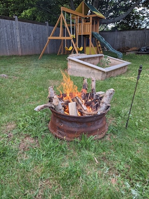 Relax by the fire pit in a serene backyard setting with a wooden play structure and a grassy lawn.