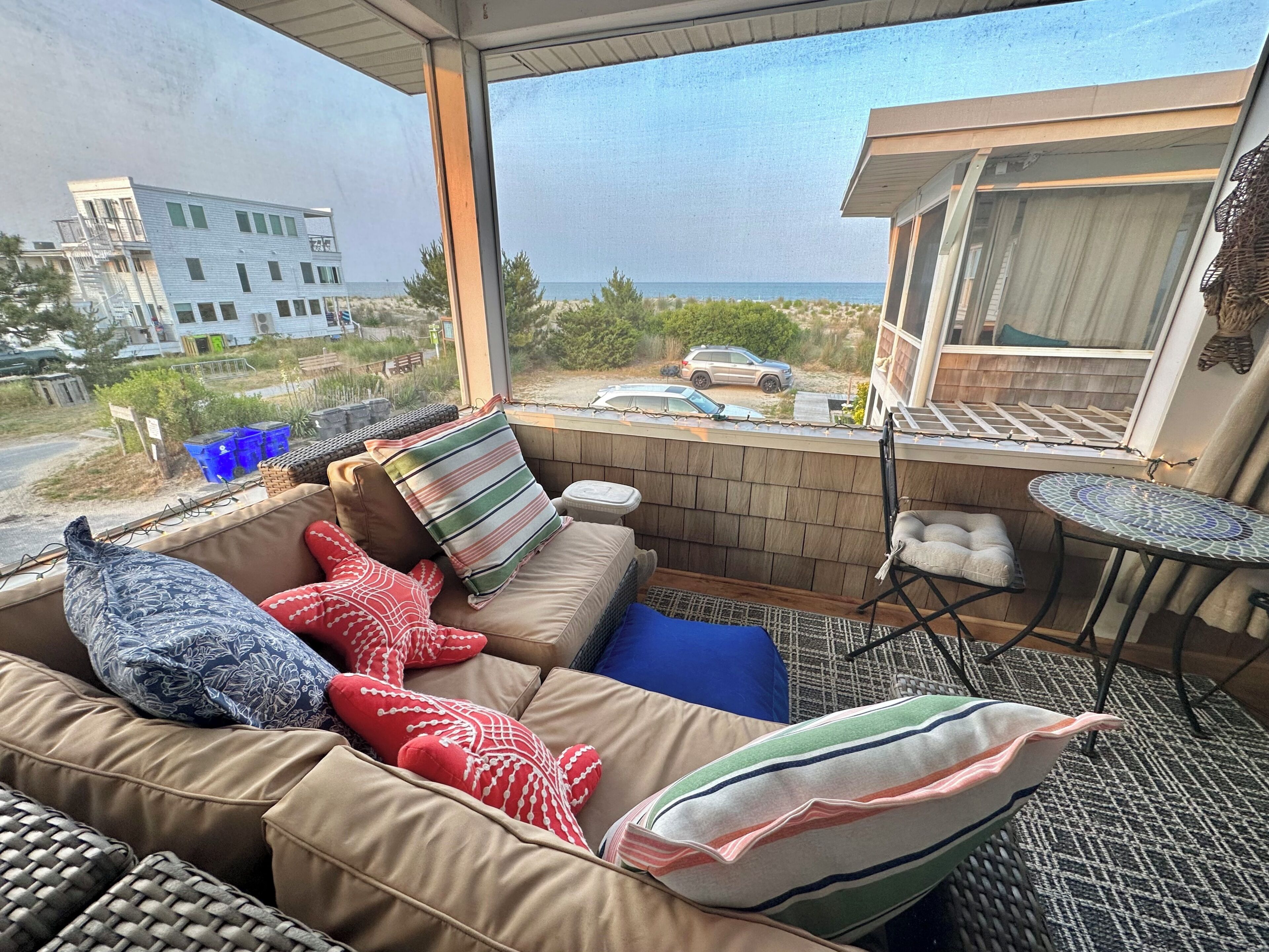 A sunlit room with a view of the beach, a sofa with patterned cushions, and a small table.