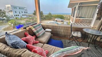 A sunlit room with a view of the beach, a sofa with patterned cushions, and a small table.