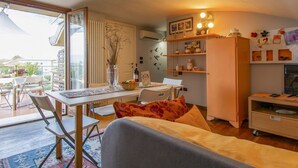 A compact living space with a dining area, a sofa, a kitchen area, and a view through a large window. - Lovely apartment for 4 guests with A/C, WIFI, TV, terrace and pets allowed (Capannori)