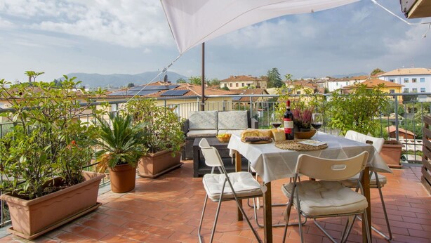 A terrace with a table set for dining, potted plants, and a view of the cityscape. - Lovely apartment for 4 guests with A/C, WIFI, TV, terrace and pets allowed (Capannori)