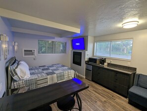 A compact bedroom with a bed, a desk, a TV, a microwave, and a small kitchenette. - Majestic Rockies Motel (Sandy)