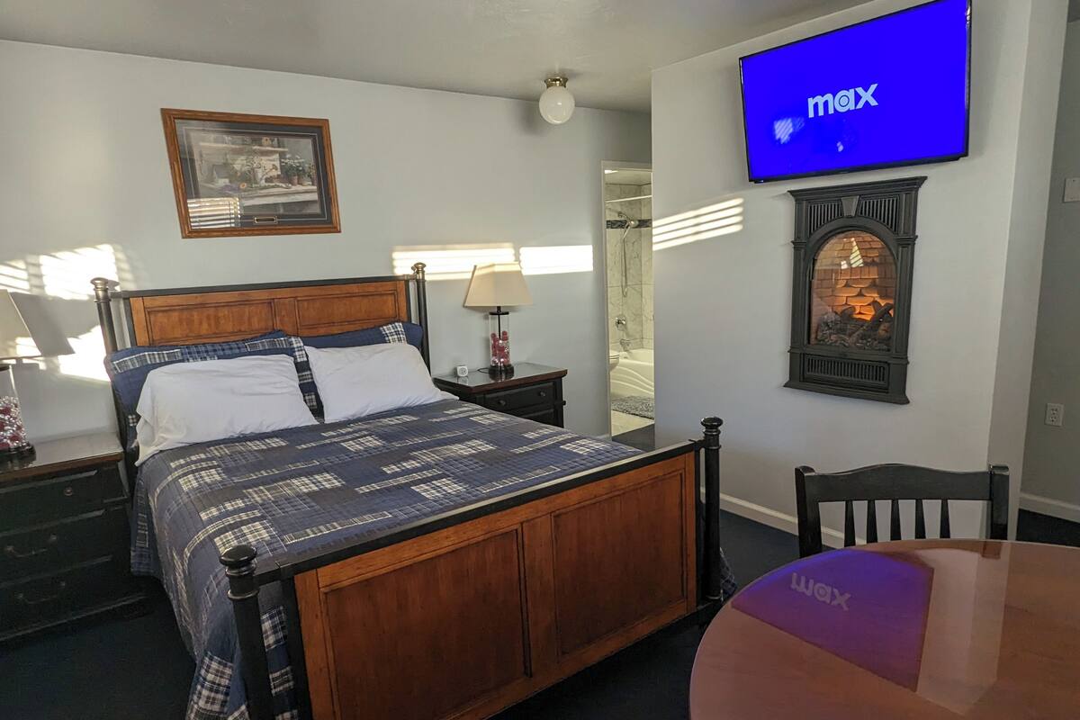 A hotel room with a bed, a TV, a fireplace, and a mirror.