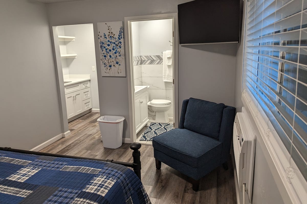 A bedroom with a bed, a chair, a TV, and a window with blinds.