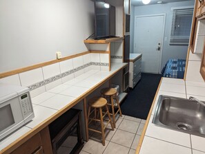 A compact kitchen with a microwave, wooden stools, a sink, and a small refrigerator. - Majestic Rockies Motel (Sandy)