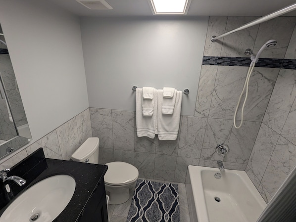 Un baño moderno con un lavamanos negro, inodoro blanco y bañera. Hay dos toallas blancas colgadas en un perchero.