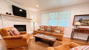 A living room with a fireplace, leather sofas, a coffee table, and a flat-screen TV mounted above the fireplace. - The Whitehouse – Louisiana Country Getaway on 8 Peaceful Acres with Pond Views (Robert)