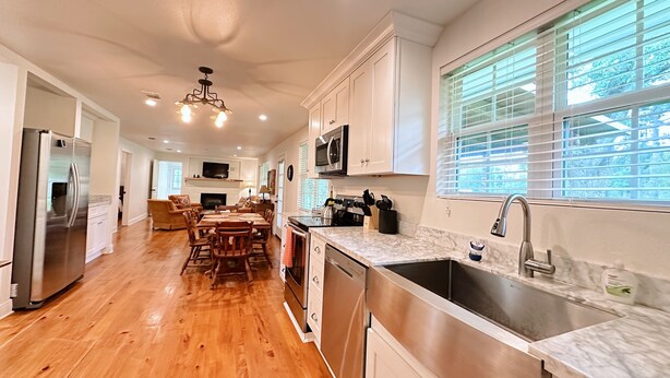 A modern kitchen with wooden flooring, stainless steel appliances, and a large window with blinds. - The Whitehouse – Louisiana Country Getaway on 8 Peaceful Acres with Pond Views (Robert)