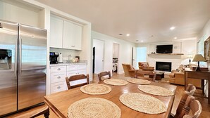 A modern kitchen with white cabinets, a stainless steel refrigerator, and a dining area with a wooden table and woven placemats. - The Whitehouse – Louisiana Country Getaway on 8 Peaceful Acres with Pond Views (Robert)