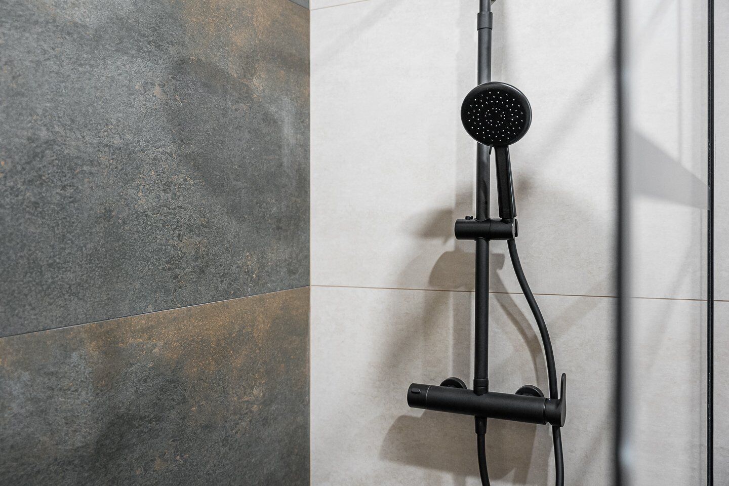 Une douche moderne dotée d’un pommeau de douche à main et d’un panneau de commande fixé au mur.