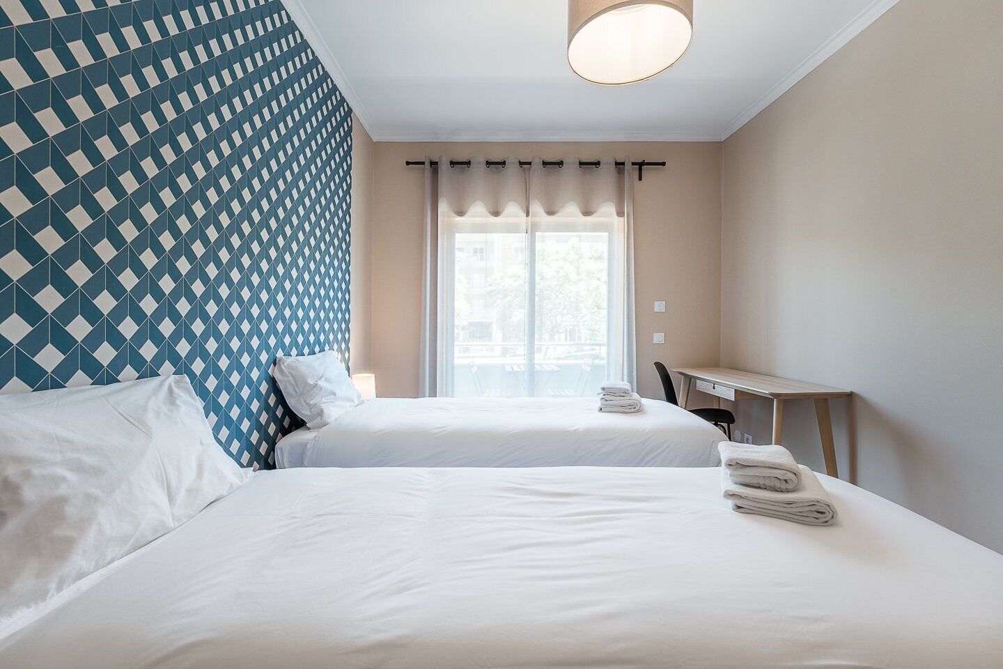 Een hotelkamer met twee bedden, een bureau en een raam met gordijnen.