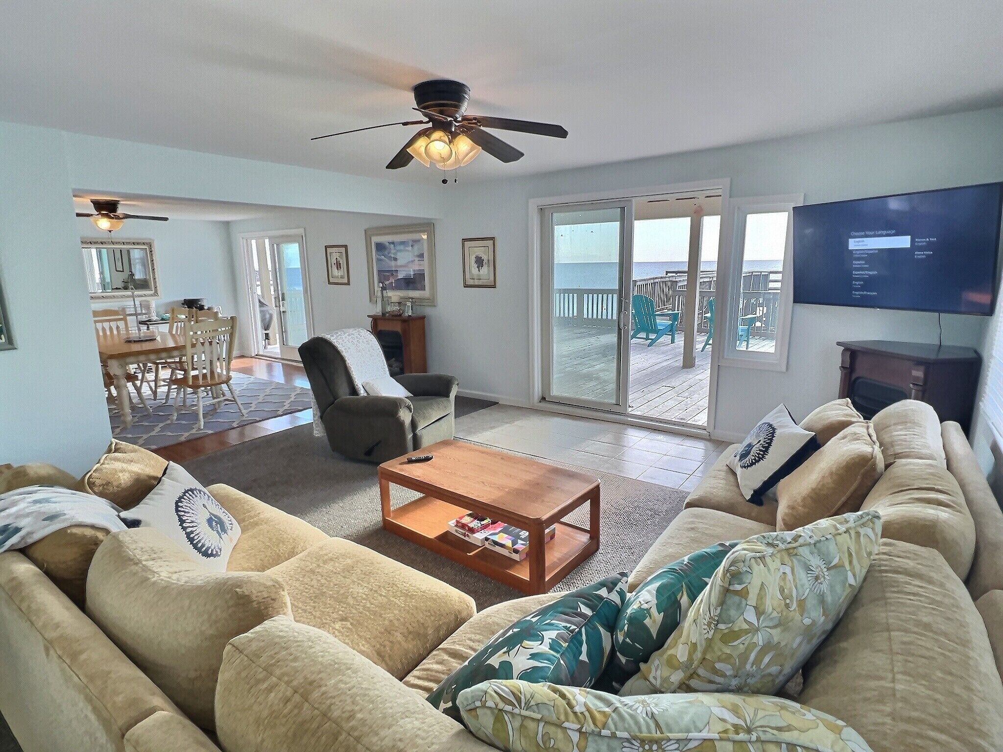 Un salon comprenant un canapé, des fauteuils, une table basse et un téléviseur. Il y a un balcon avec vue sur la plage.