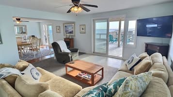 Un salon comprenant un canapé, des fauteuils, une table basse et un téléviseur. Il y a un balcon avec vue sur la plage.