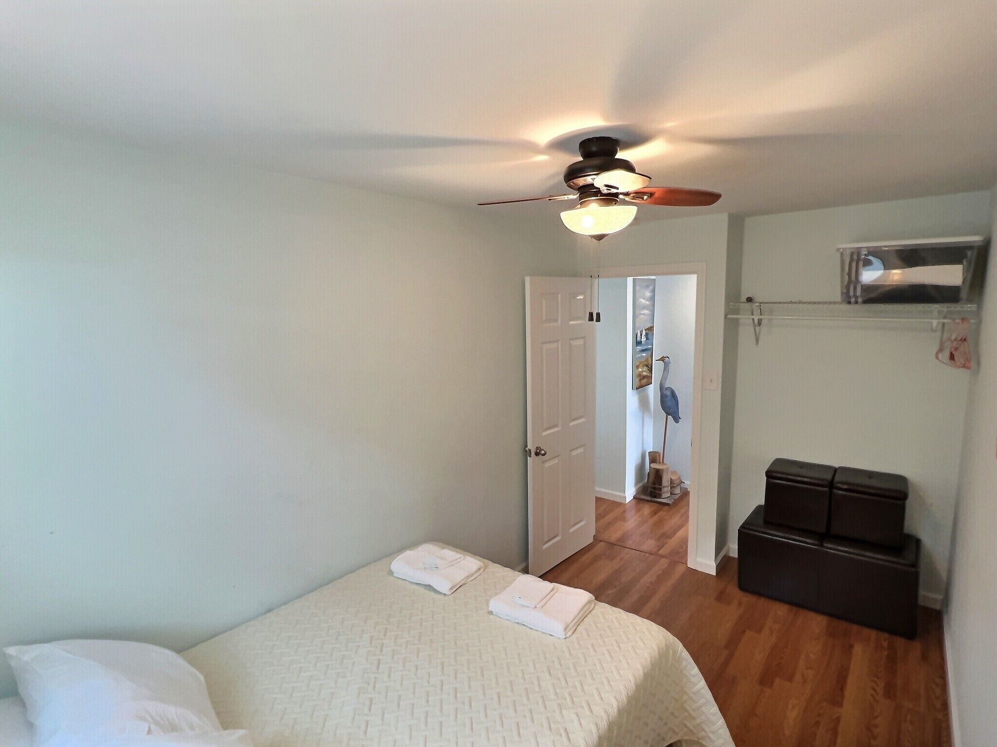 Un dormitorio con cama, ventilador de techo, una puerta blanca y un pasillo que conduce a otra habitación.