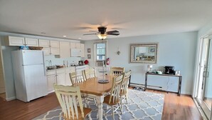 A modern kitchen with white cabinets, a dining table with chairs, a ceiling fan, and a kitchen island. - Reed's Beach - Stunning waterfront Sunsets - Bay Front Home Steps to beach (Middle Township)