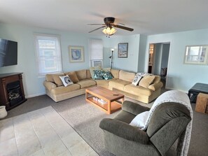 A living room with a beige sectional sofa, a wooden coffee table, a grey armchair, and a ceiling fan. - Reed's Beach - Stunning waterfront Sunsets - Bay Front Home Steps to beach (Middle Township)