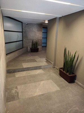 A hallway with a tiled floor, a potted plant, and a wall with a frosted glass panel. - Amazing 2BR in Parque España (Mexico City)