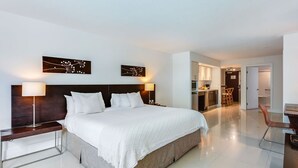 A modern hotel room with a large bed, two bedside lamps, a nightstand, and a view into the kitchen area. - Accessible Studio with King Size Bed Kitchenette, Steps Away from Bal Harbour Beach (Bal Harbour)