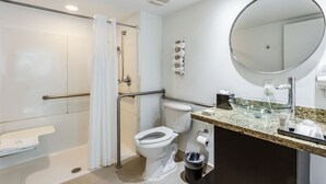 A modern bathroom with a glass shower enclosure, a toilet, a sink with a granite countertop, and a large mirror. - Accessible Studio with King Size Bed Kitchenette, Steps Away from Bal Harbour Beach (Bal Harbour)