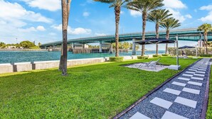 A waterfront patio with palm trees, a pool, and a bridge in the background. - Accessible Studio with King Size Bed Kitchenette, Steps Away from Bal Harbour Beach (Bal Harbour)