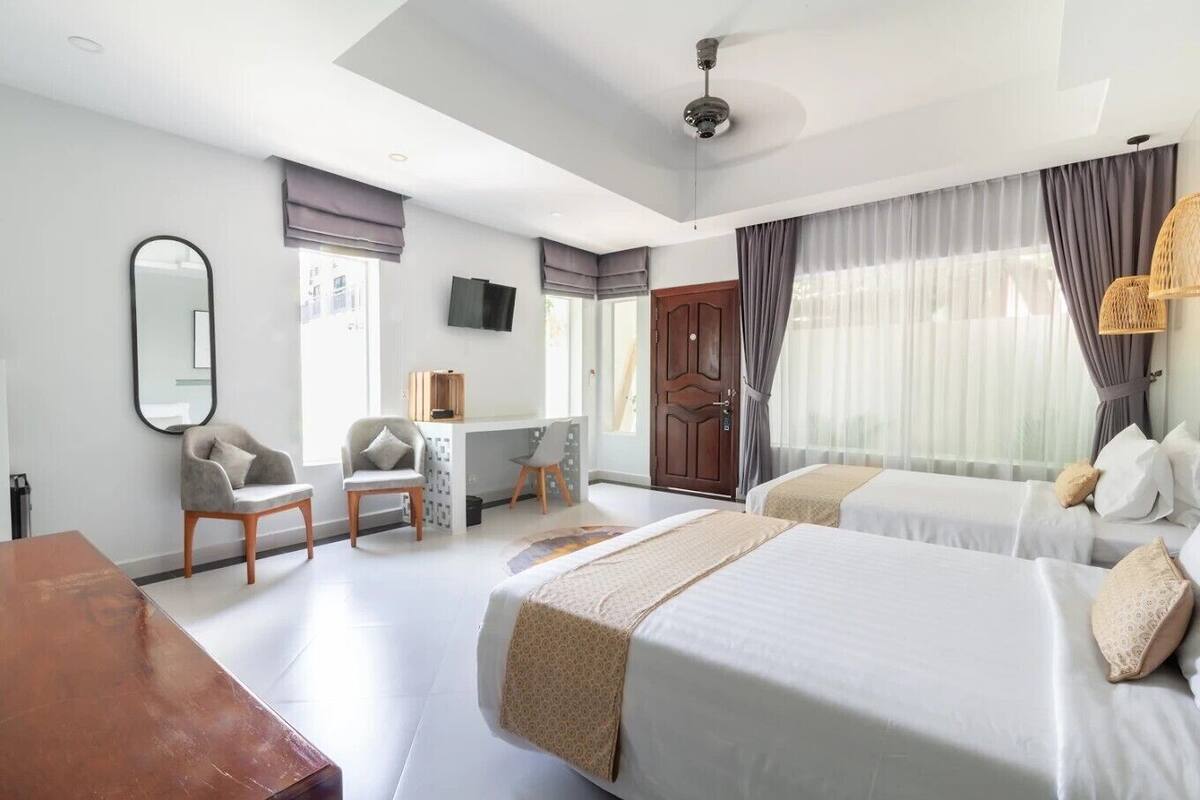 Habitación de hotel con dos camas, un escritorio, una silla, un televisor y un ventanal grande con cortinas.