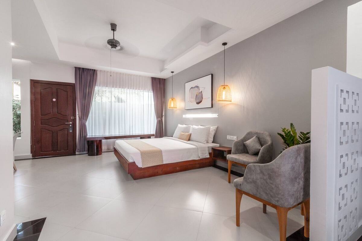 Un dormitorio moderno con una cama grande, mesitas de noche, una silla y un ventilador de techo.