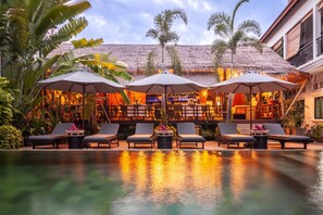 A poolside area with lounge chairs and umbrellas, a bar with a thatched roof, and tropical plants. - La bastide de Caro (Siem Reap)