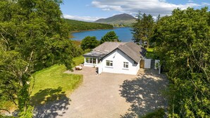 A white house with a sloped roof, a gravel driveway, and a view of a lake and mountains. - Cottage 446 - Letterfrack - sleeps 6 guests  in 3 bedrooms (Letterfrack)