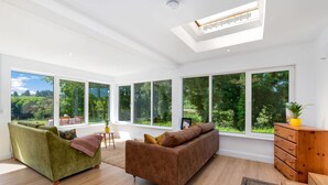 A spacious living room with large windows, a green sofa, a brown sofa, and a wooden dresser. - Cottage 446 - Letterfrack - sleeps 6 guests  in 3 bedrooms (Letterfrack)
