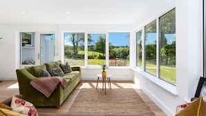 A modern living room with a green sofa, a brown sofa, and a small table with a plant. Large windows offer a view of a garden and a dining area. - Cottage 446 - Letterfrack - sleeps 6 guests  in 3 bedrooms (Letterfrack)