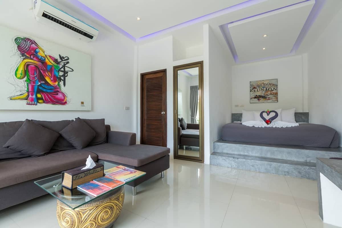 Un dormitorio moderno con cama, sofá, una mesita de centro de vidrio y aire acondicionado instalado en la pared.