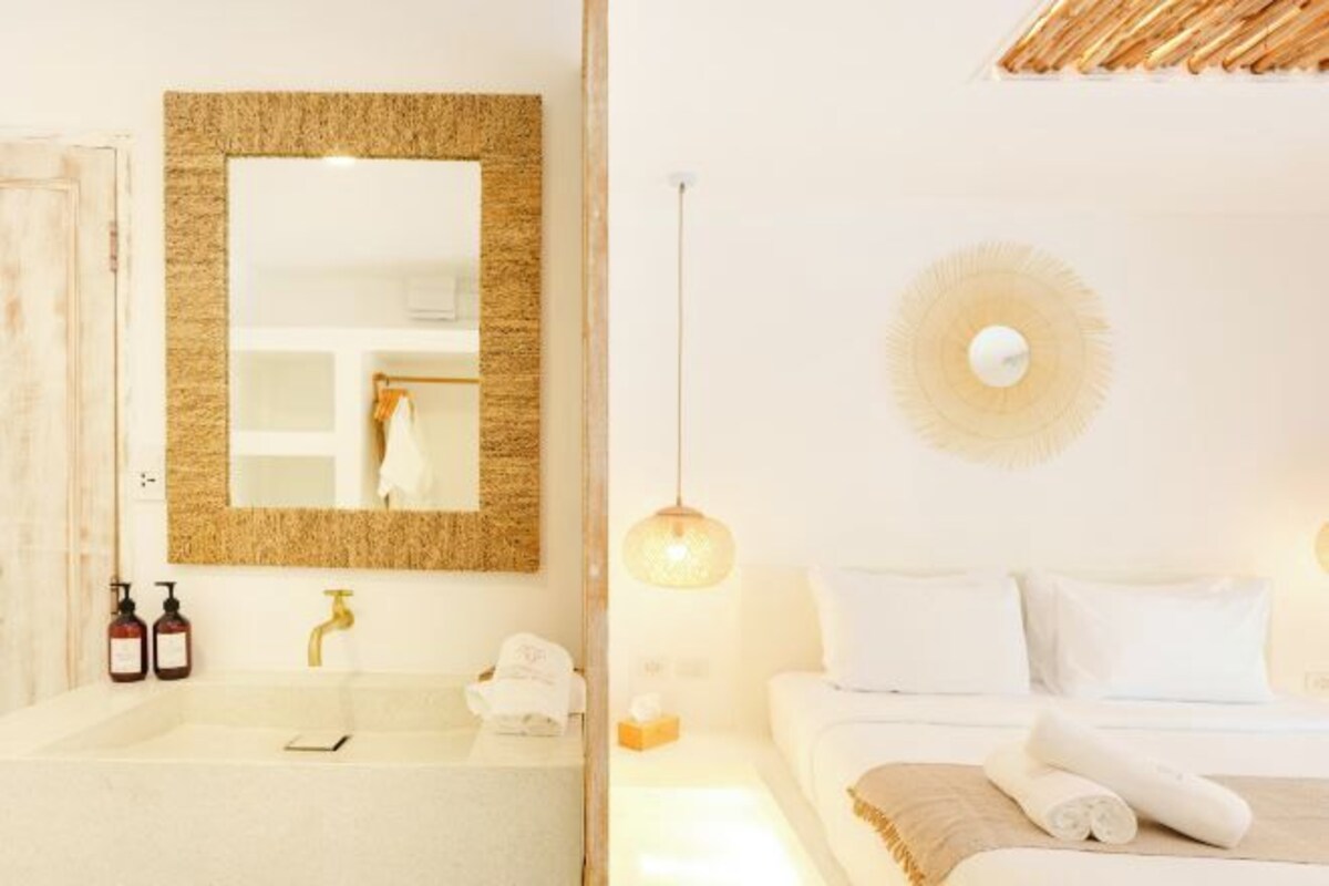 Habitación de hotel con un espejo grande, una bañera, una cama con ropa blanca y un aplique de pared.