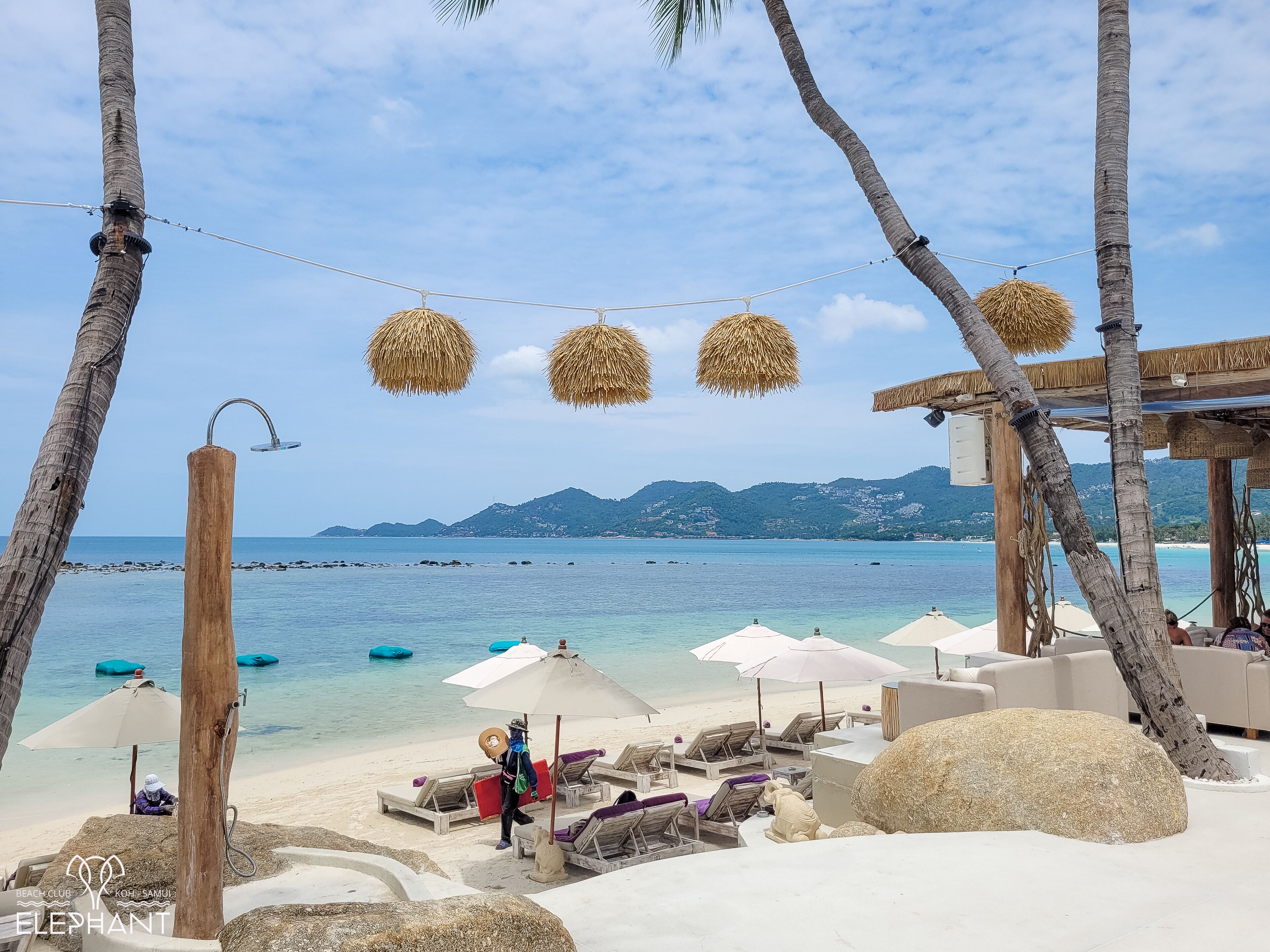 Un espace de détente aménagé sur la plage, avec des chaises longues, des parasols et une vue sur la mer et les montagnes.
