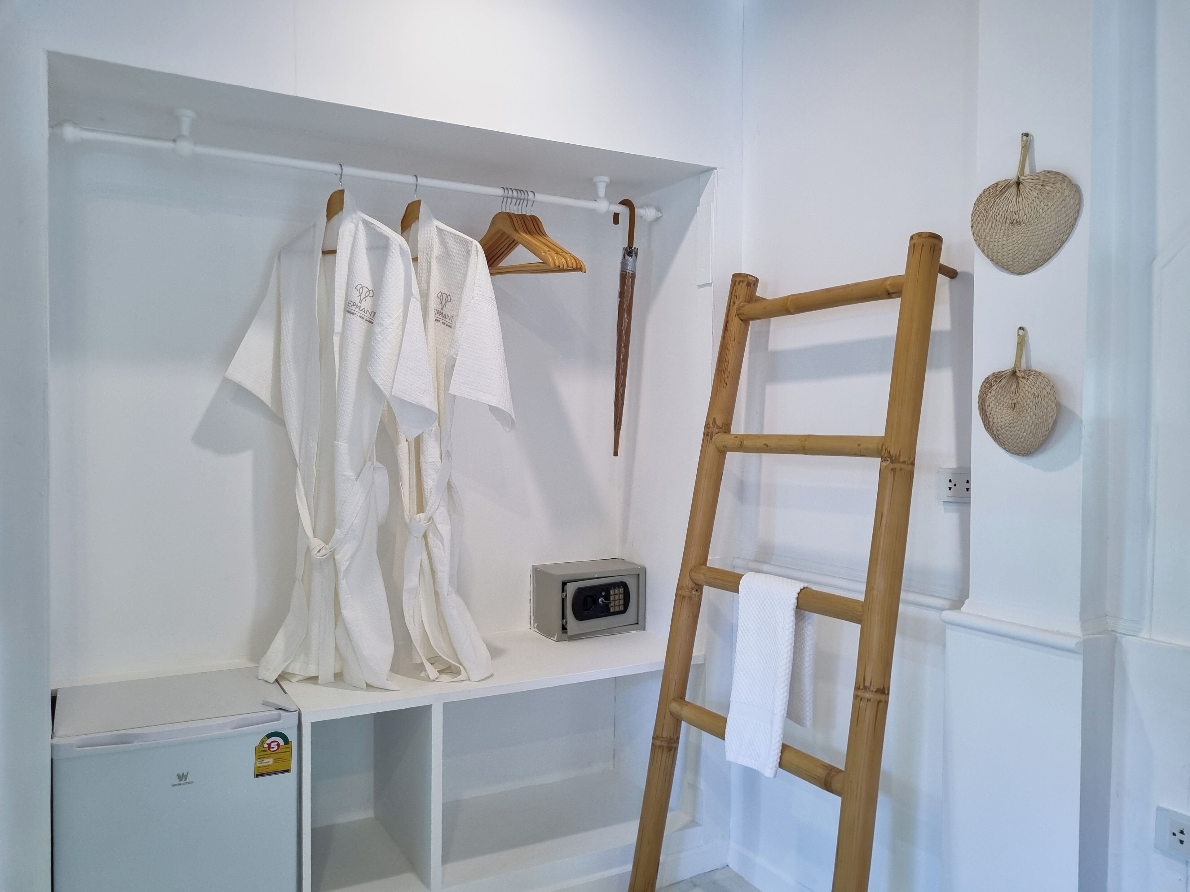A white closet with hanging clothes, a wooden ladder, and a small appliance.