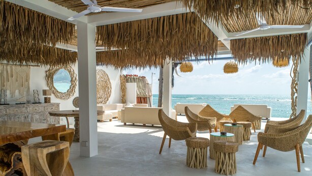 Een strandlounge met rieten meubilair, een grote houten tafel en uitzicht op de oceaan.