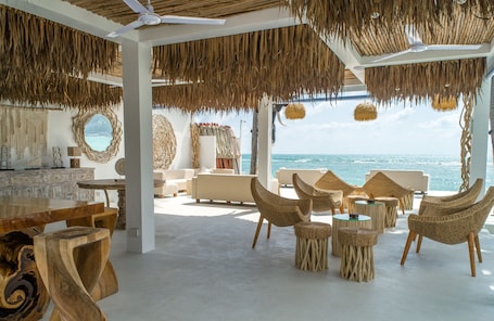 A beachside lounge with wicker furniture, a large wooden table, and a view of the ocean.