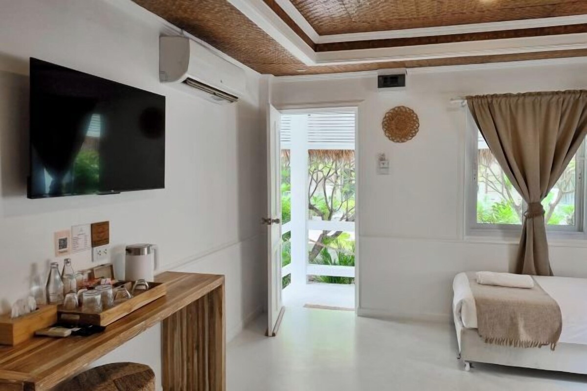 Quarto com cama, televisão, mesa consola de madeira e janela com cortinas.