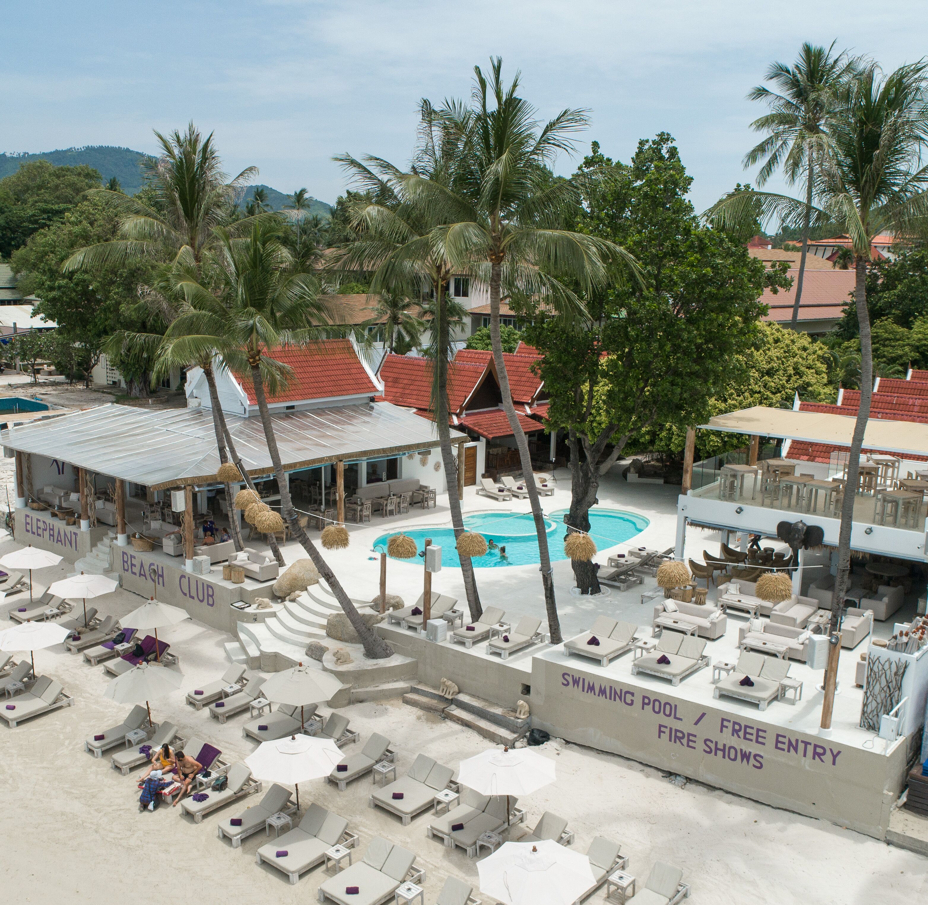 A resort with a swimming pool, lounge chairs, and palm trees.