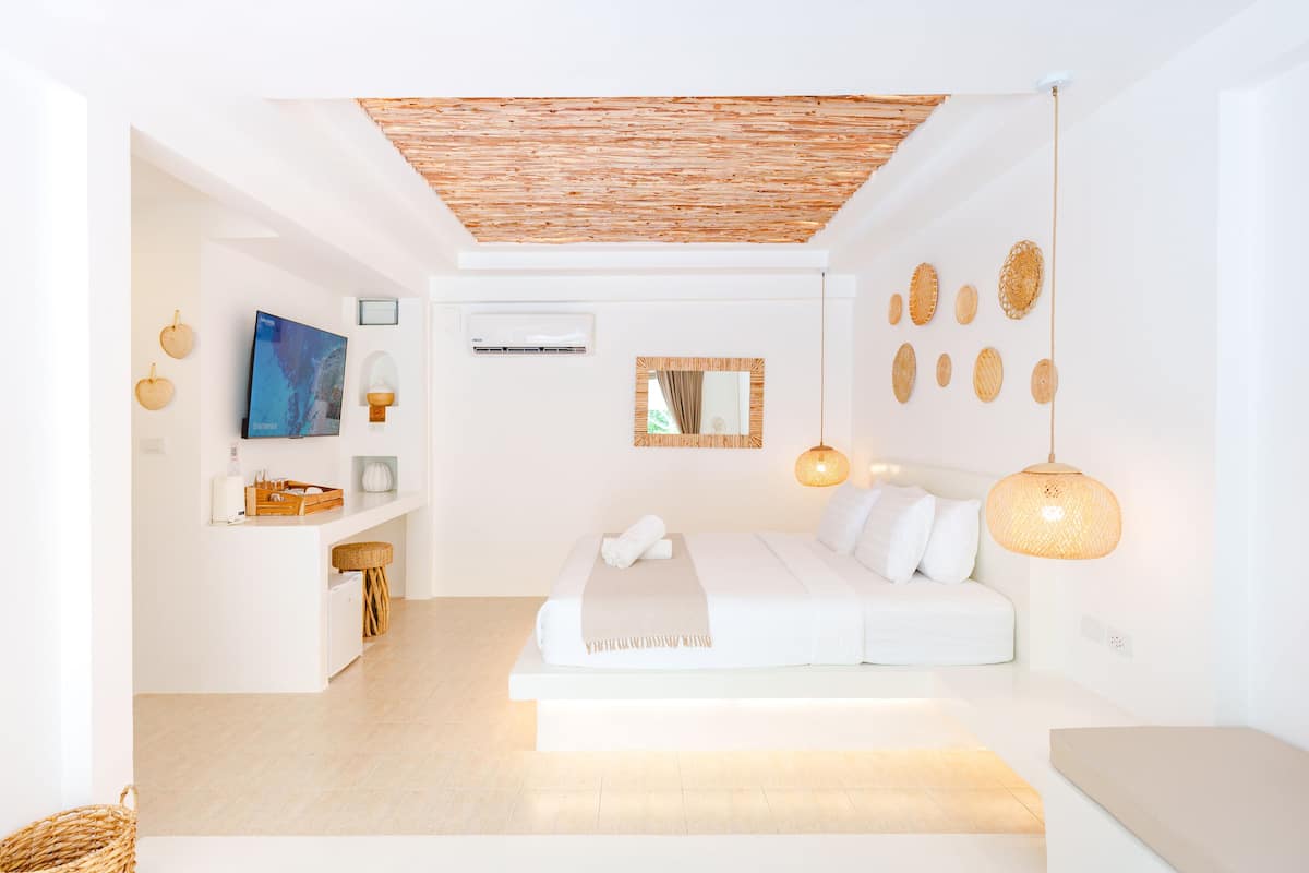Un dormitorio moderno con una cama grande, televisor, un pequeño rincón de descanso y un techo con textura de madera.