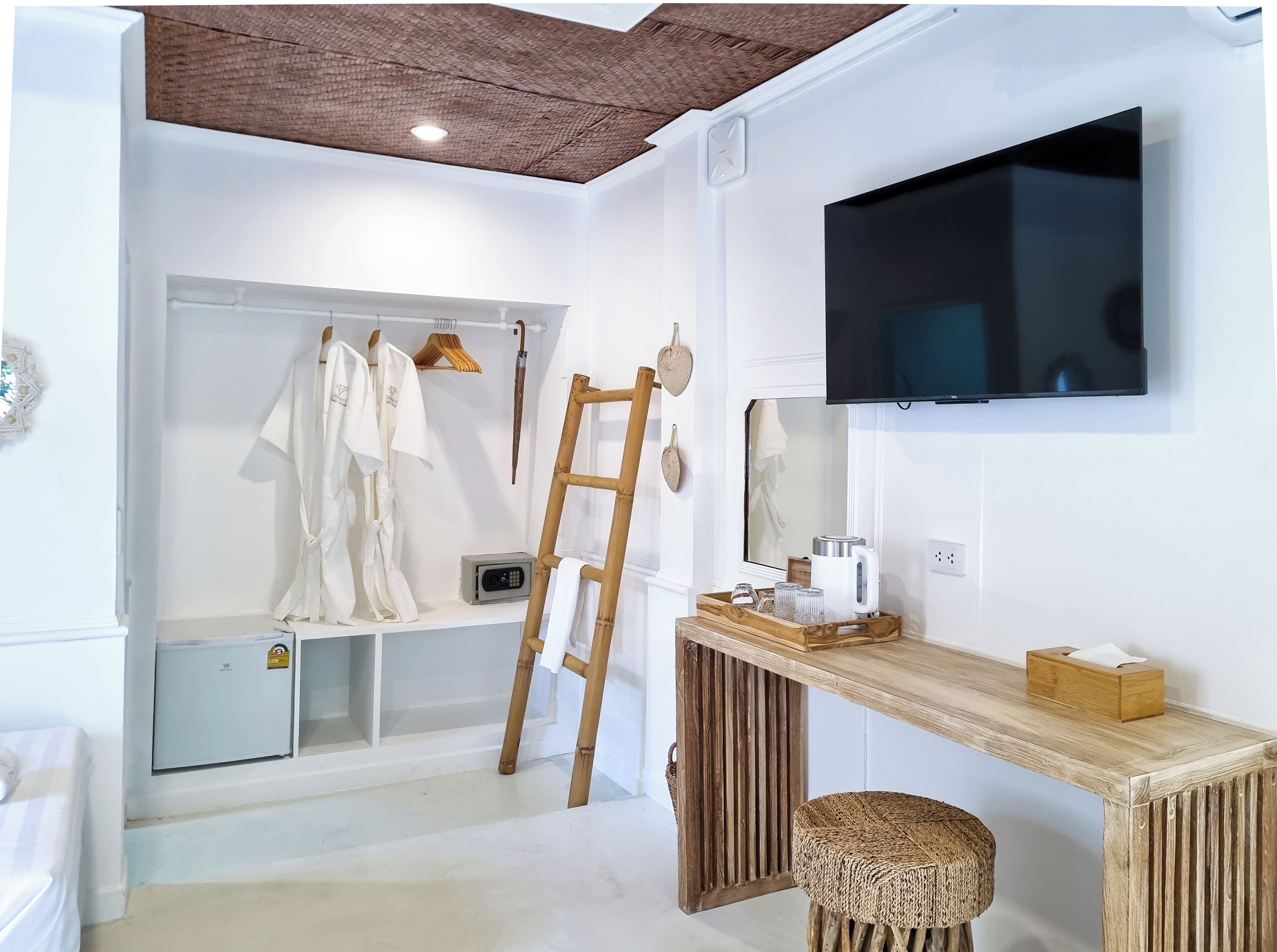 A modern bathroom with a wooden ceiling, a mounted TV, a vanity with a wooden stool, and a towel rack with robes.