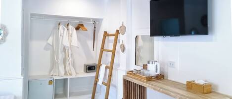 A modern bathroom with a wooden ceiling, a mounted TV, a vanity with a wooden stool, and a towel rack with robes.