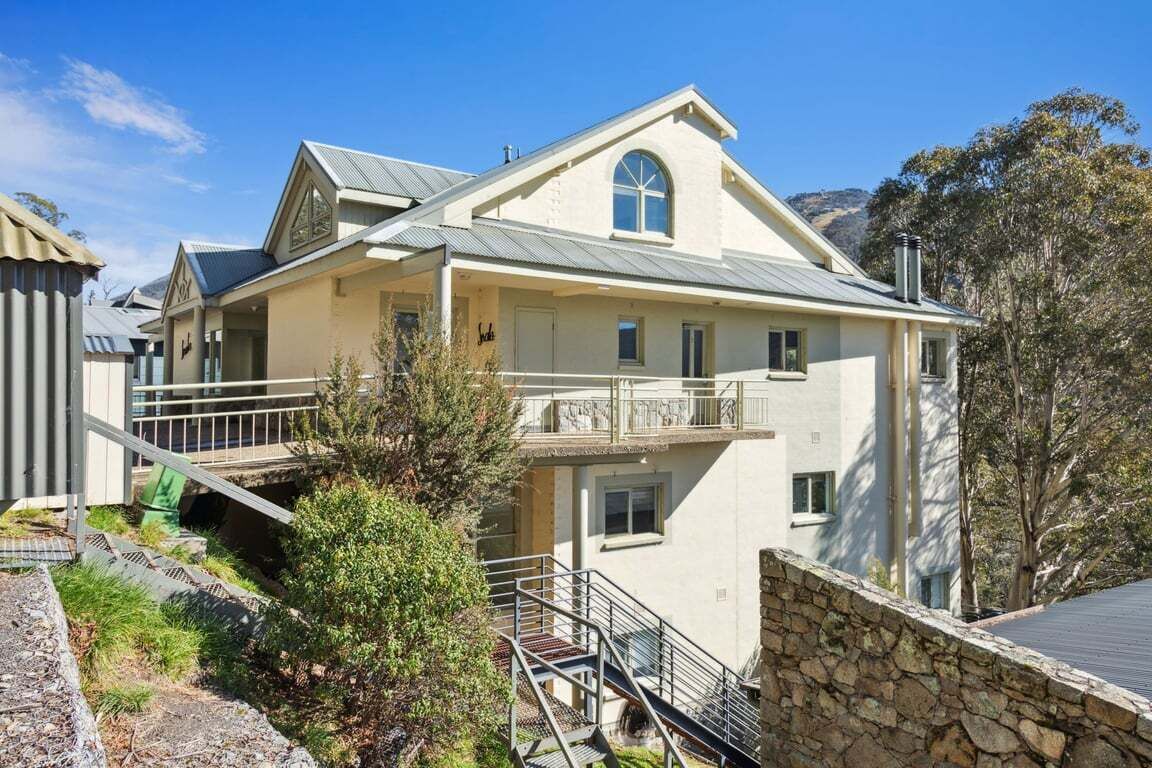 Ein zweistöckiges Gebäude mit einem Balkon, einer steinernen Stützmauer und einer Treppe, die zum Eingang führt.